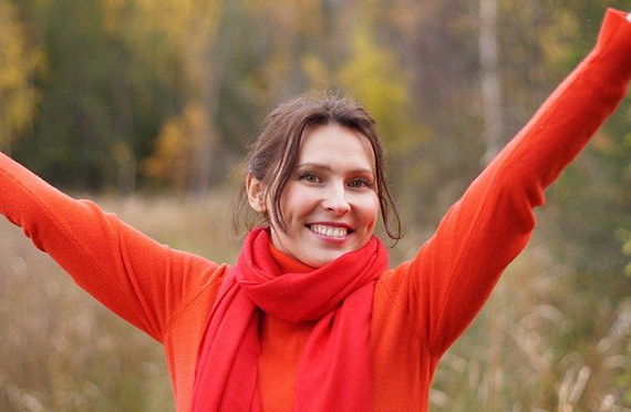 Photo of woman with arms raised in triumph and happiness standing in a meadow with trees in the background