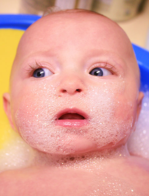 Photo of a cute baby with wide open eyes and fun cleansing bubbles around their face. 